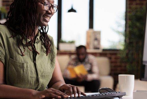 Lady in the living room all smiles while working, typing on her keyboard | Madison Life Insurance