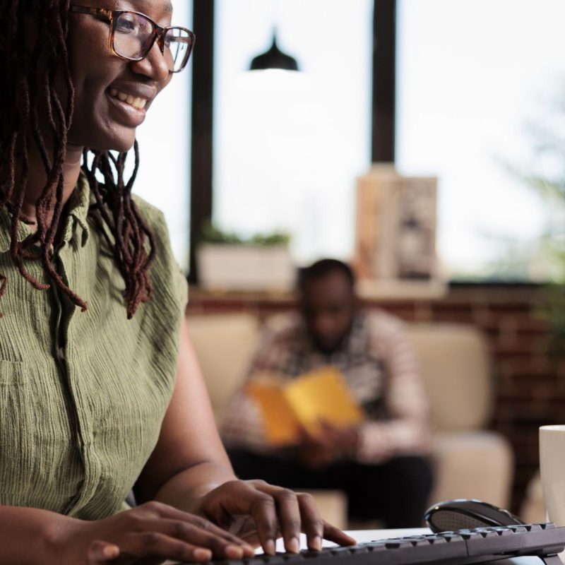 Lady in the living room all smiles while working, typing on her keyboard